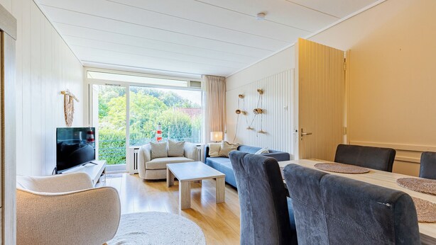 A modern living room with a sofa, chairs, a TV, and a dining area with a table and chairs.