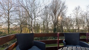Ein Außenbereich mit Korbstühlen und einem Holztisch, umgeben von einer Holzterrasse und Blick auf kahlstehende Bäume.