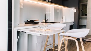 A modern kitchen with white countertops, wooden stools, and a built-in stove. - 96 Riverfront Apartment (Đà Nẵng)