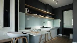 A modern kitchen with white countertops, wooden stools, and a built-in island. - 96 Riverfront Apartment (Đà Nẵng)