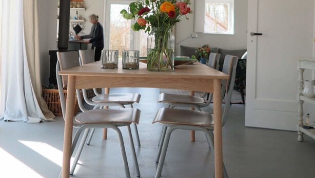 A dining area with a wooden table, four chairs, a vase with flowers, and a window with a view.