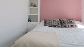 A bedroom with a bed, a bedside table, a shelf with items, and a wardrobe.