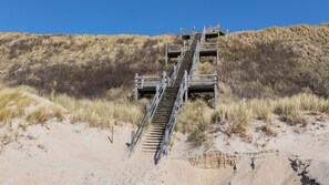 Eine Holztreppe führt einen sandigen Hügel hinauf, oben befindet sich eine Aussichtsplattform aus Holz.