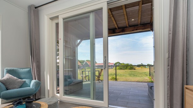 Un soggiorno moderno con un divano color petrolio, un tavolino in legno e una porta scorrevole in vetro che si apre su un patio con vista su una proprietà recintata.