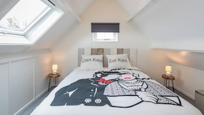 Una camera da letto con soffitto spiovente, una finestra a lucernario, un letto con copripiumino decorato, due lampade da comodino e una piccola finestra sopra il letto.