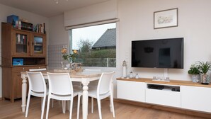 Une cuisine moderne avec une table à manger, des chaises, un téléviseur et une fenêtre donnant sur une maison.