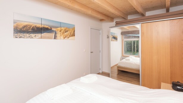 Une chambre avec un plafond en bois, un lit, une armoire et une grande fenêtre.