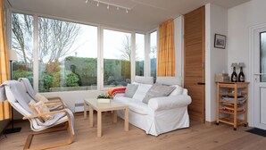 Un salon moderne avec un canapé blanc, une chaise en bois, une petite table et une bibliothèque.