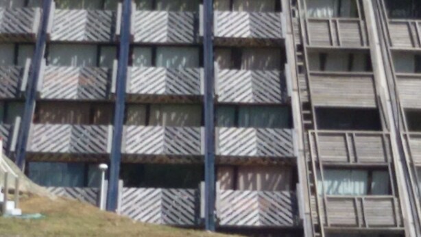 Un edifici de diverses plantes amb una façana característica d'estil escamot, amb balcons i una escala central.