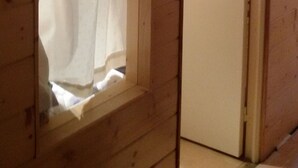 Une pièce avec une fenêtre recouverte d’un rideau blanc, une porte en bois et un mur en bois apparent.