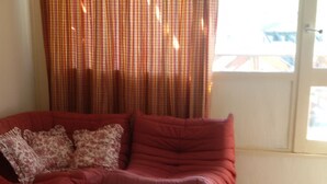 Un salon avec un canapé rouge, une table basse blanche et une fenêtre avec des rideaux.