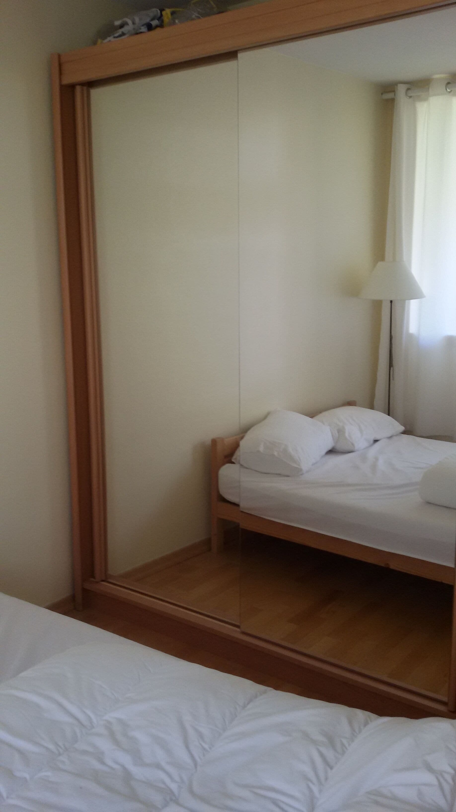 A bedroom with a bed, a wooden wardrobe, and a mirror.