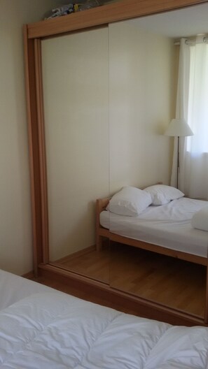 A bedroom with a bed, a wooden wardrobe, and a mirror.