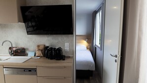 Une chambre d’hôtel compacte comprenant un coin cuisine, un lit et un téléviseur fixé au mur.