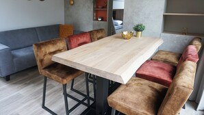 Un coin repas avec une table en bois et des chaises rembourrées, un canapé gris et une petite plante posée sur la table.
