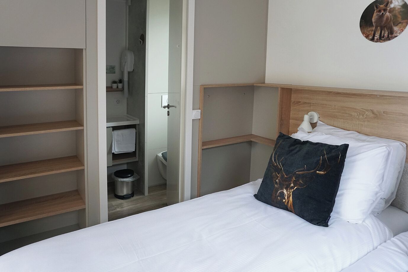 A bedroom with a bed, a wooden headboard, a nightstand, a wall-mounted picture, and a closet with shelves.