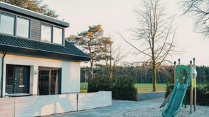 Una casa moderna con un patio, un tobogán y un parque infantil.