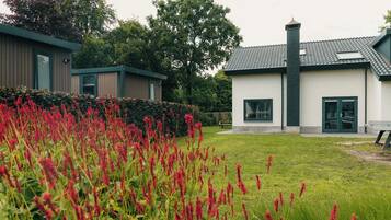 A modern building with a white exterior and dark roof tiles, surrounded by a well-maintained lawn and red flowering plants.