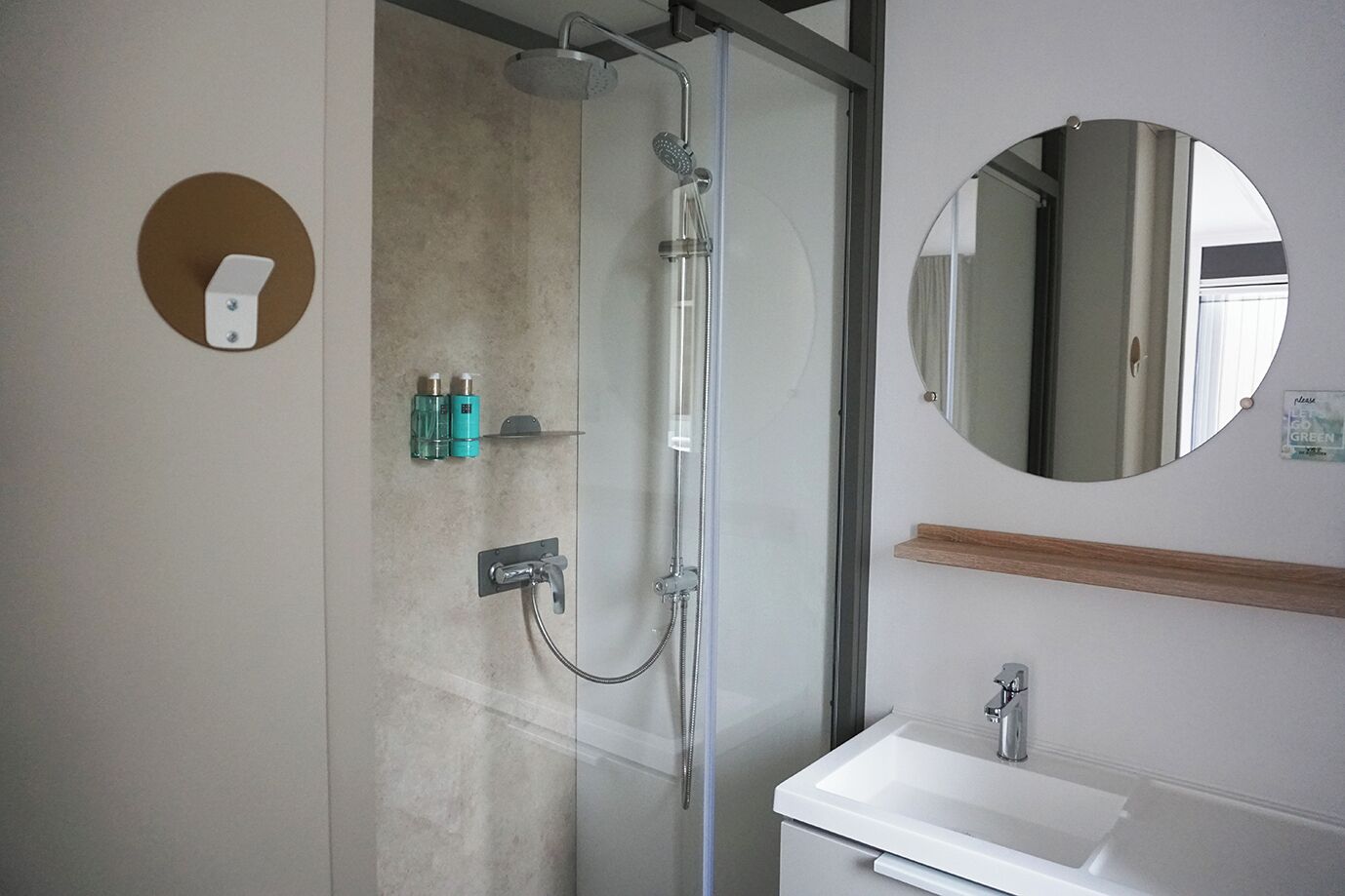 A modern bathroom with a glass-enclosed shower, a white sink, and a round mirror.