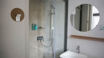 A modern bathroom with a glass-enclosed shower, a white sink, and a round mirror.