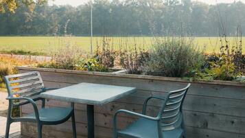 An outdoor seating area with a table and two chairs, surrounded by a wooden planter with various plants.