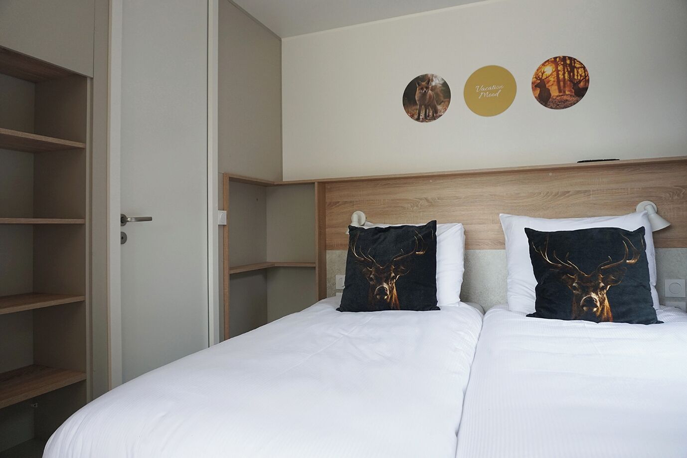 Een hotelkamer met een groot bed, twee kussens met hertenmotieven, een houten hoofdbord en een muur met drie ronde decoraties.