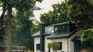 Una casa moderna con fachada blanca y detalles oscuros, rodeada de abundante vegetación y un jardín.