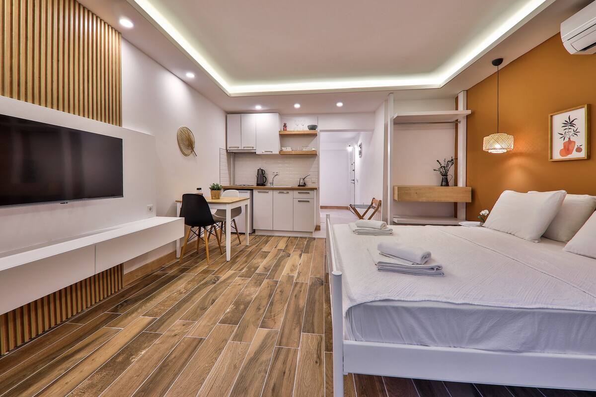 A modern hotel room with a flat-screen TV, a bed, a desk, and a kitchenette.
