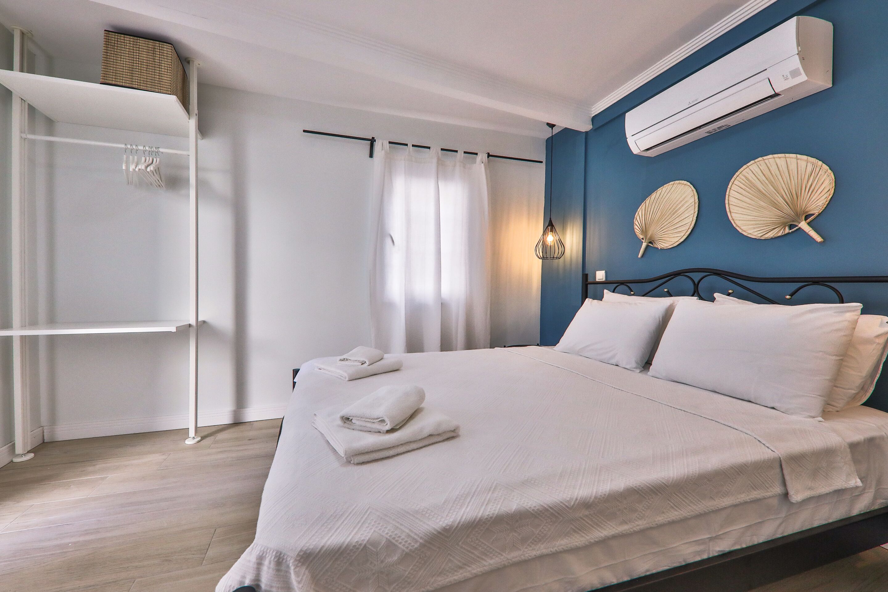 A bedroom with a bed, white towels, a wardrobe, an air conditioner, and decorative fans on the wall.