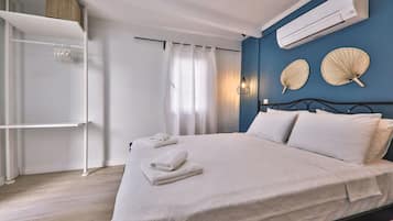 A bedroom with a bed, white towels, a wardrobe, an air conditioner, and decorative fans on the wall.