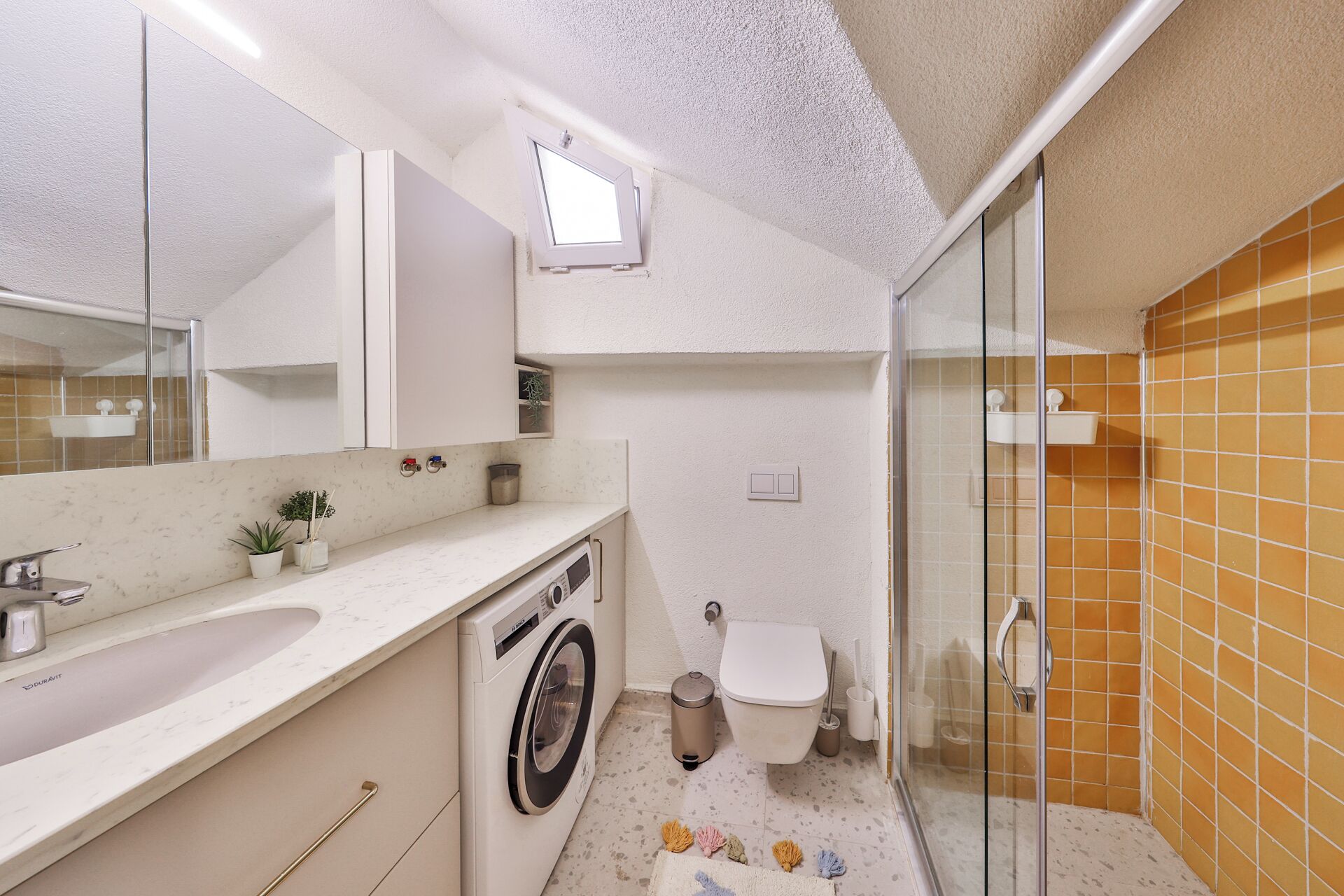 Un baño con lavadora, inodoro, lavamanos y zona de ducha.