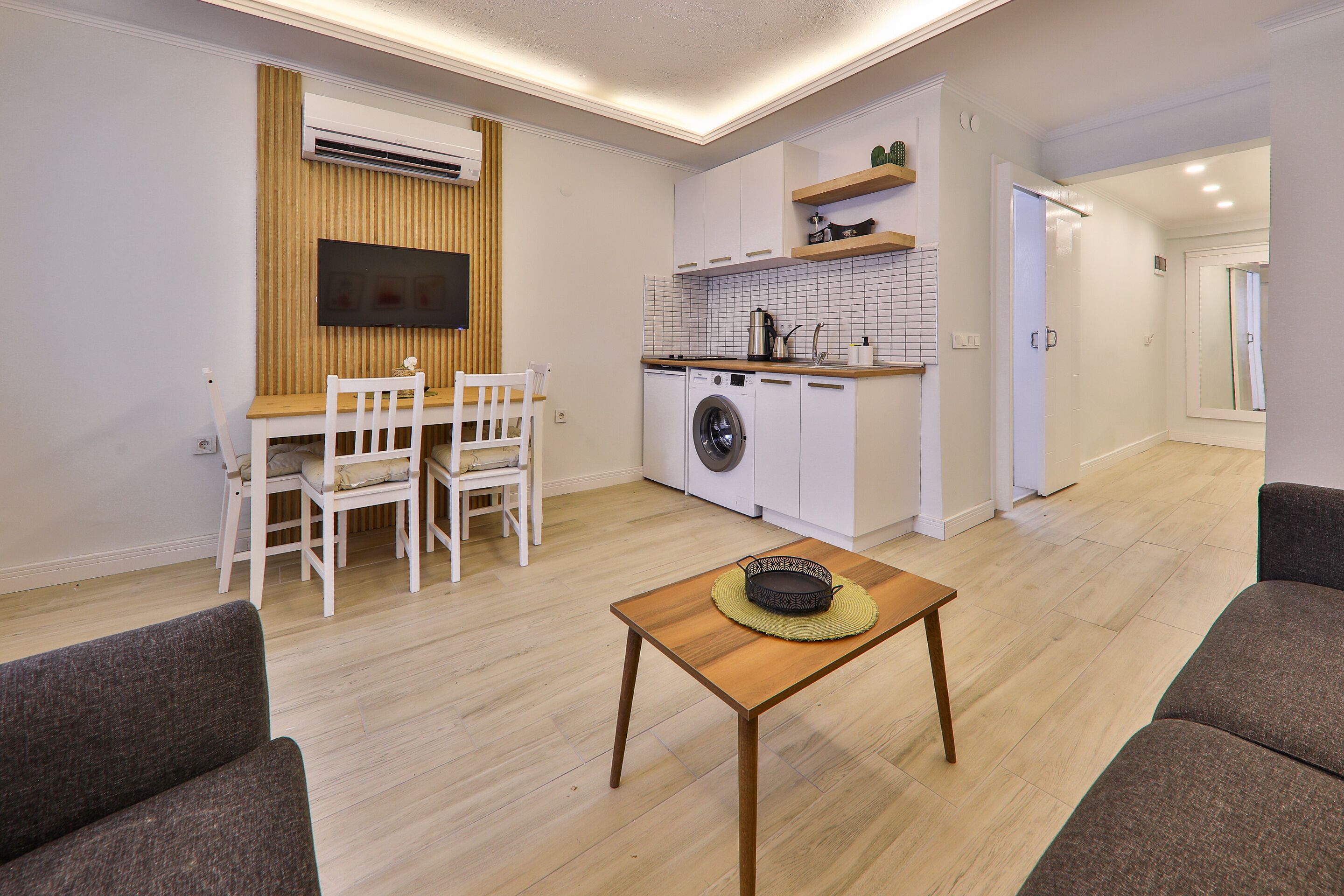 A compact living space with a dining area, a washing machine, and a kitchenette.