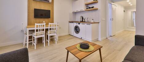 A compact living space with a dining area, a washing machine, and a kitchenette.
