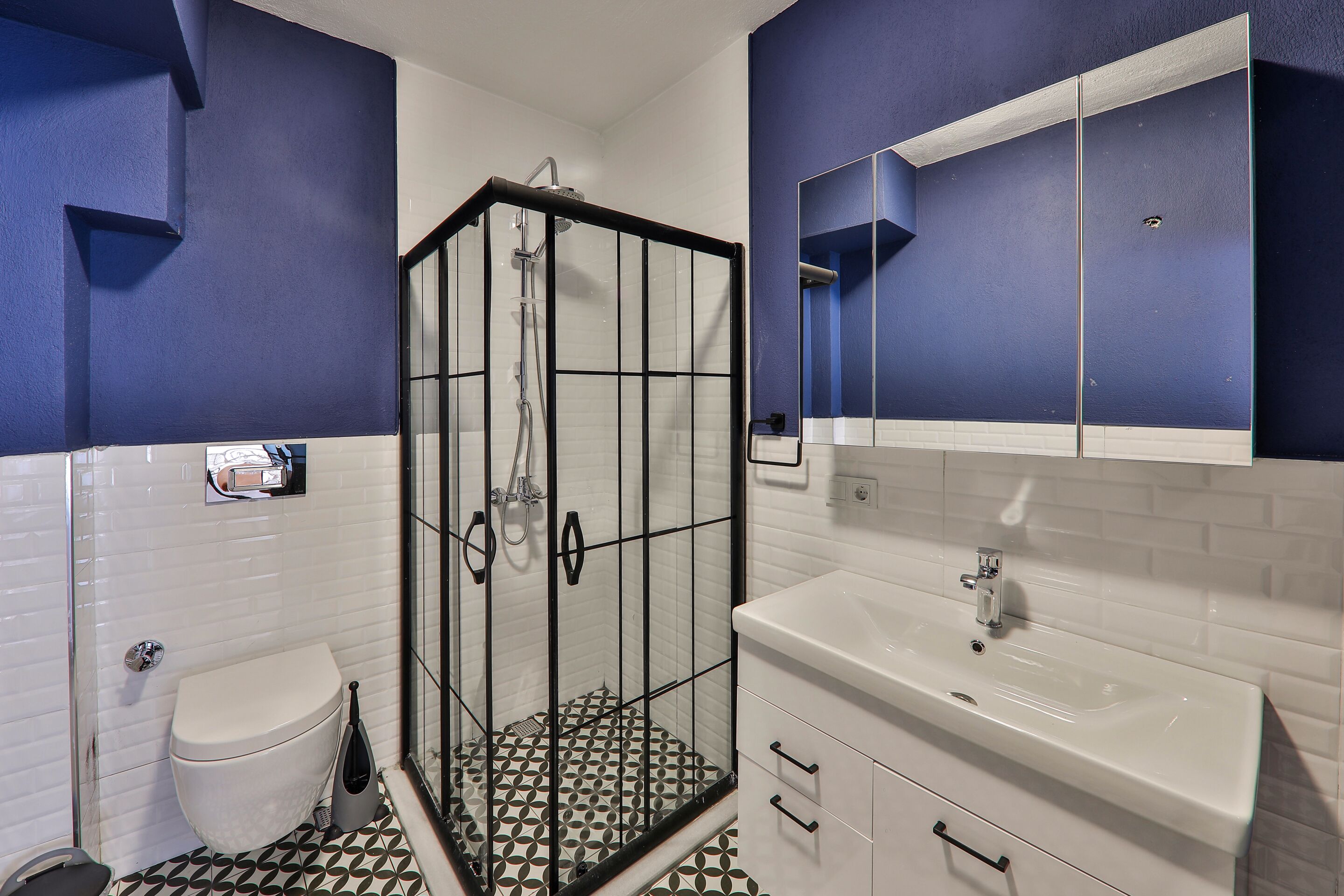 A bathroom with a glass-enclosed shower, a white toilet, and a sink with a mirror above it.