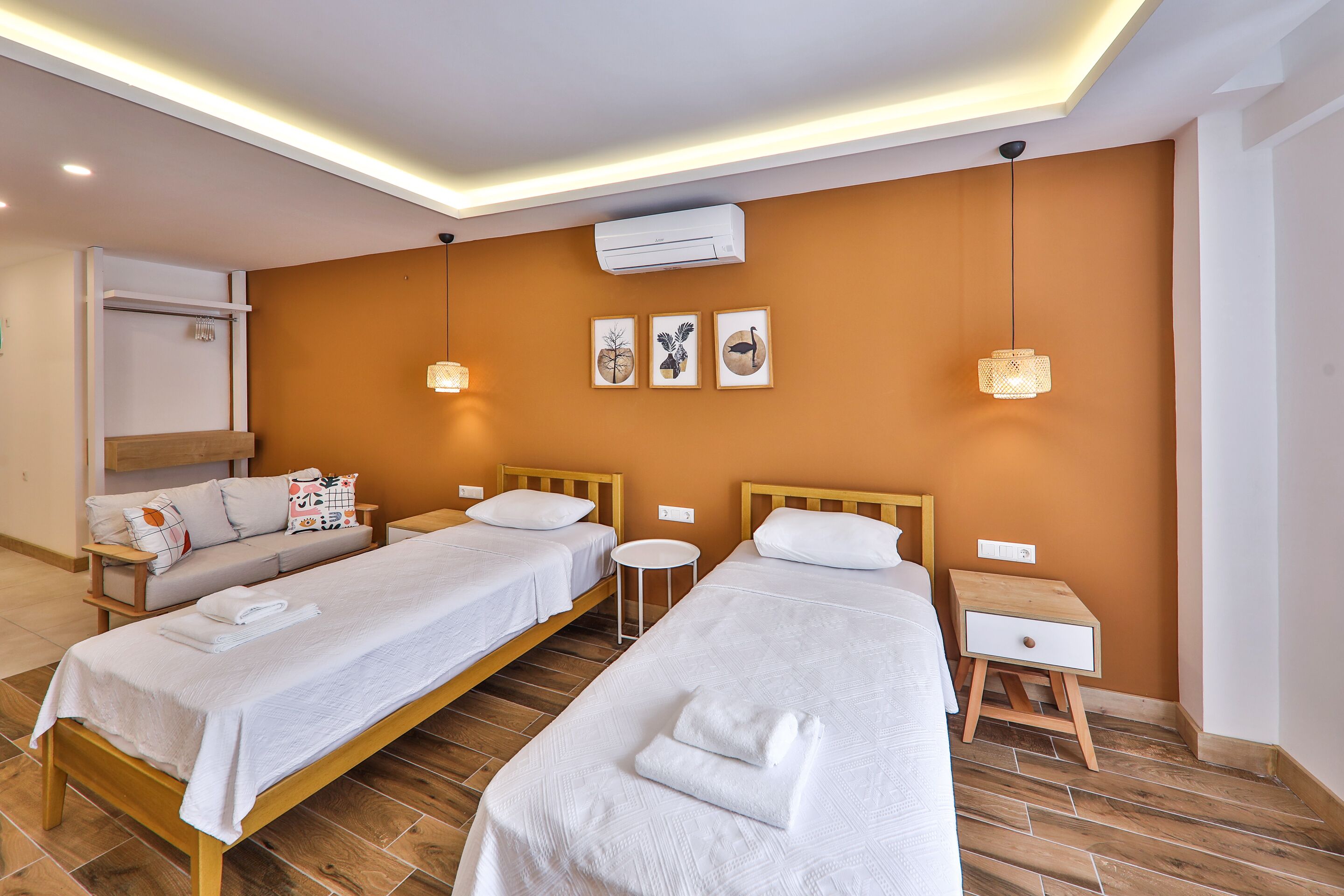 A hotel room with two beds, a sofa, a small round table, and a wall-mounted air conditioner.