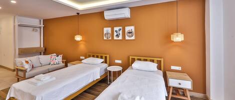 A hotel room with two beds, a sofa, a small round table, and a wall-mounted air conditioner.