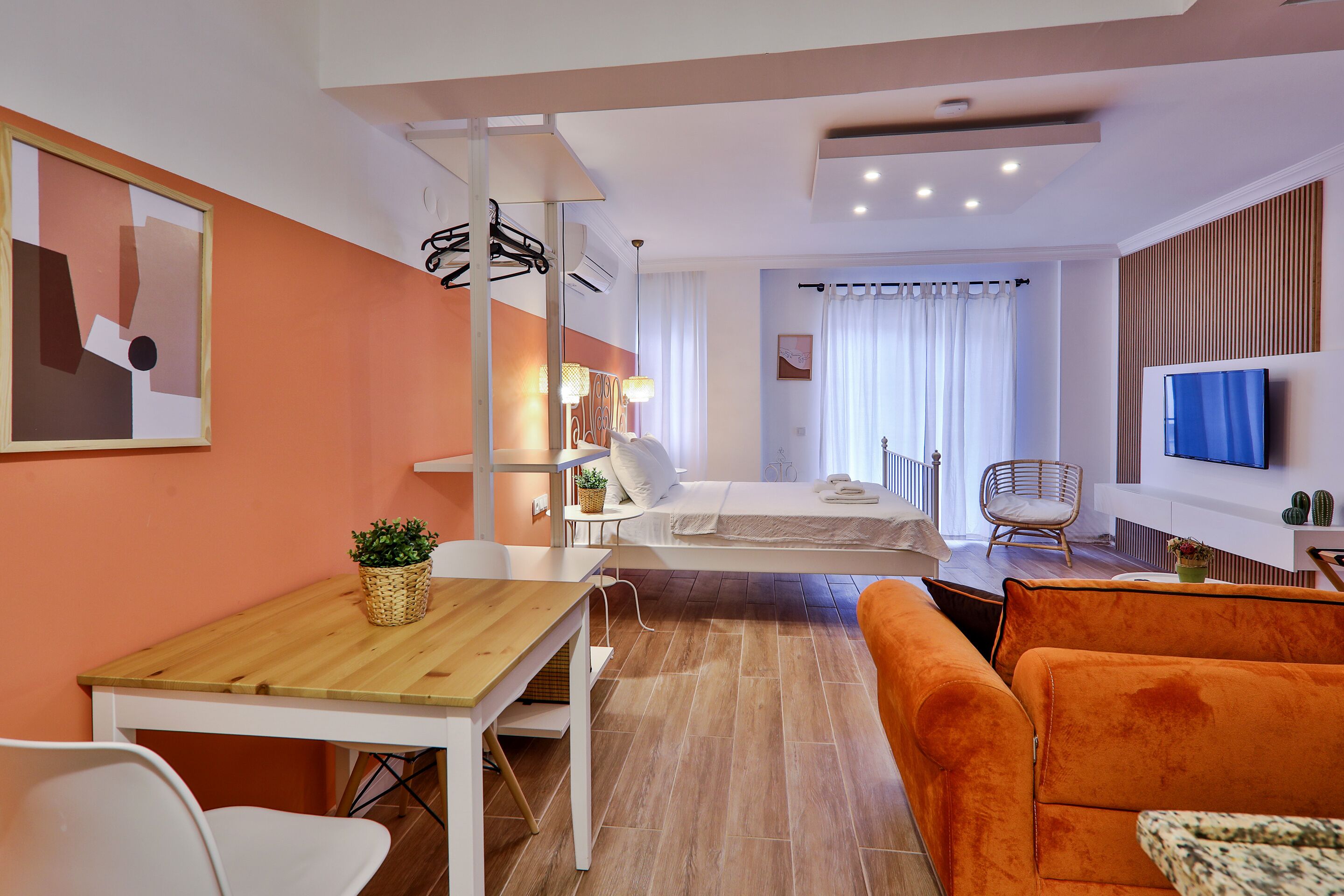 A modern hotel room with a wooden table, orange sofa, and a bed with white bedding.