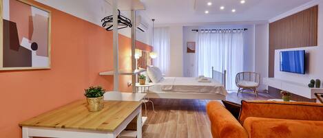 A modern hotel room with a wooden table, orange sofa, and a bed with white bedding.