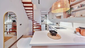 A modern kitchen with white countertops, a central island, and a wooden spiral staircase.