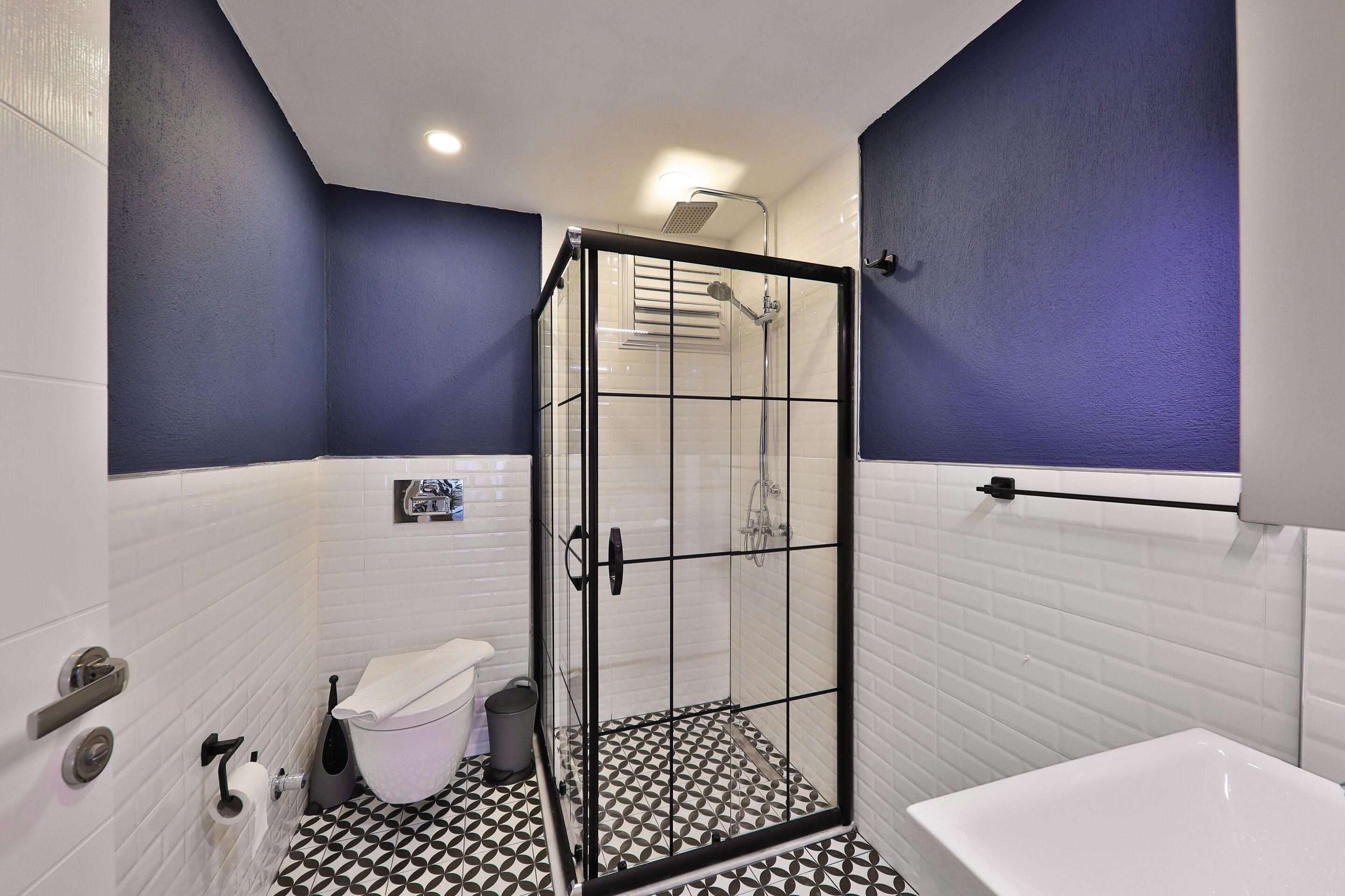 A bathroom with a glass-enclosed shower, white tiled walls, and a patterned floor.