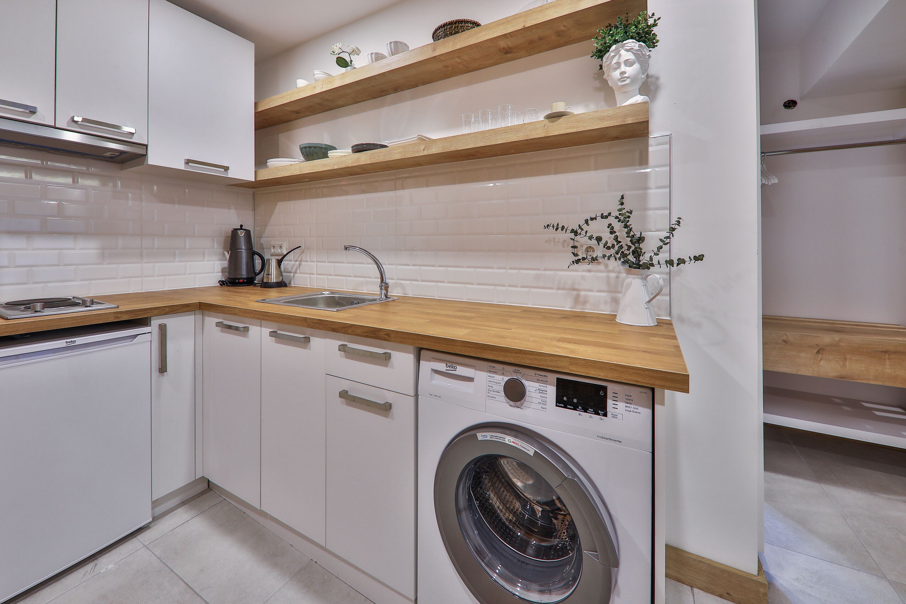 Une cuisine moderne avec des meubles blancs, un plan de travail en bois, un lave-linge encastré et un évier.