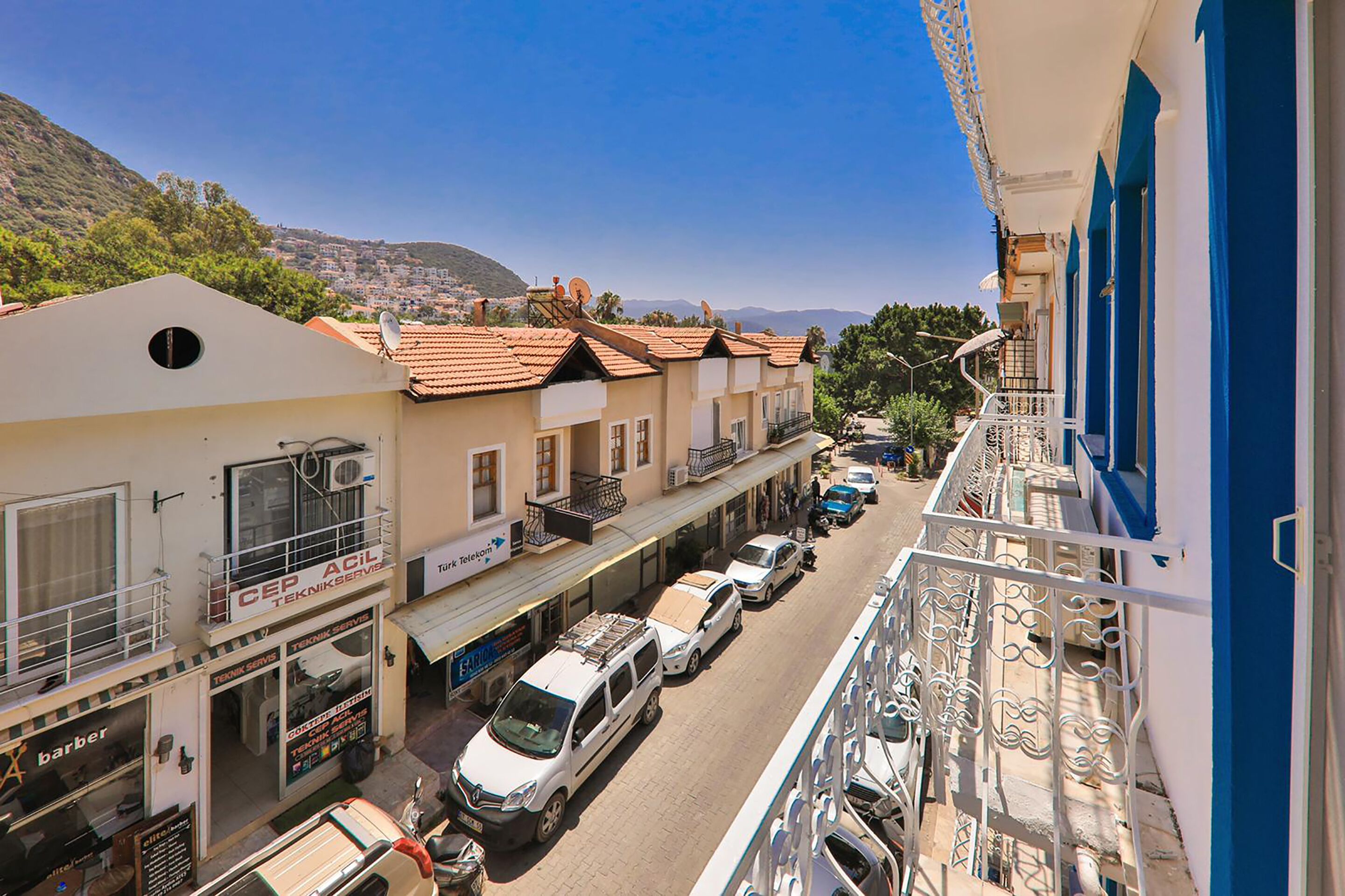 A street view with buildings, parked cars, and a balcony with railings.