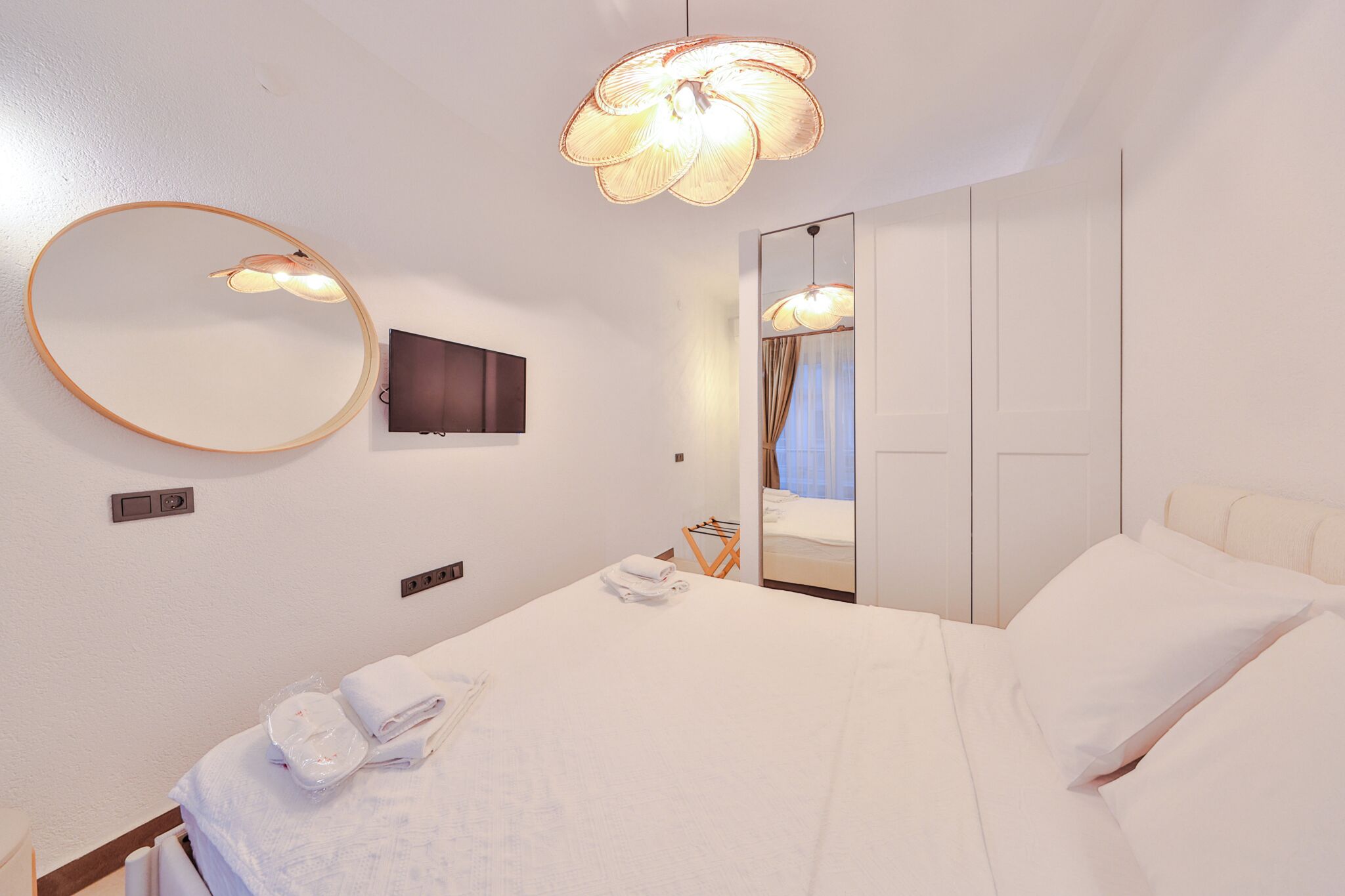 A hotel room with a bed, a TV, a mirror, and a light fixture.