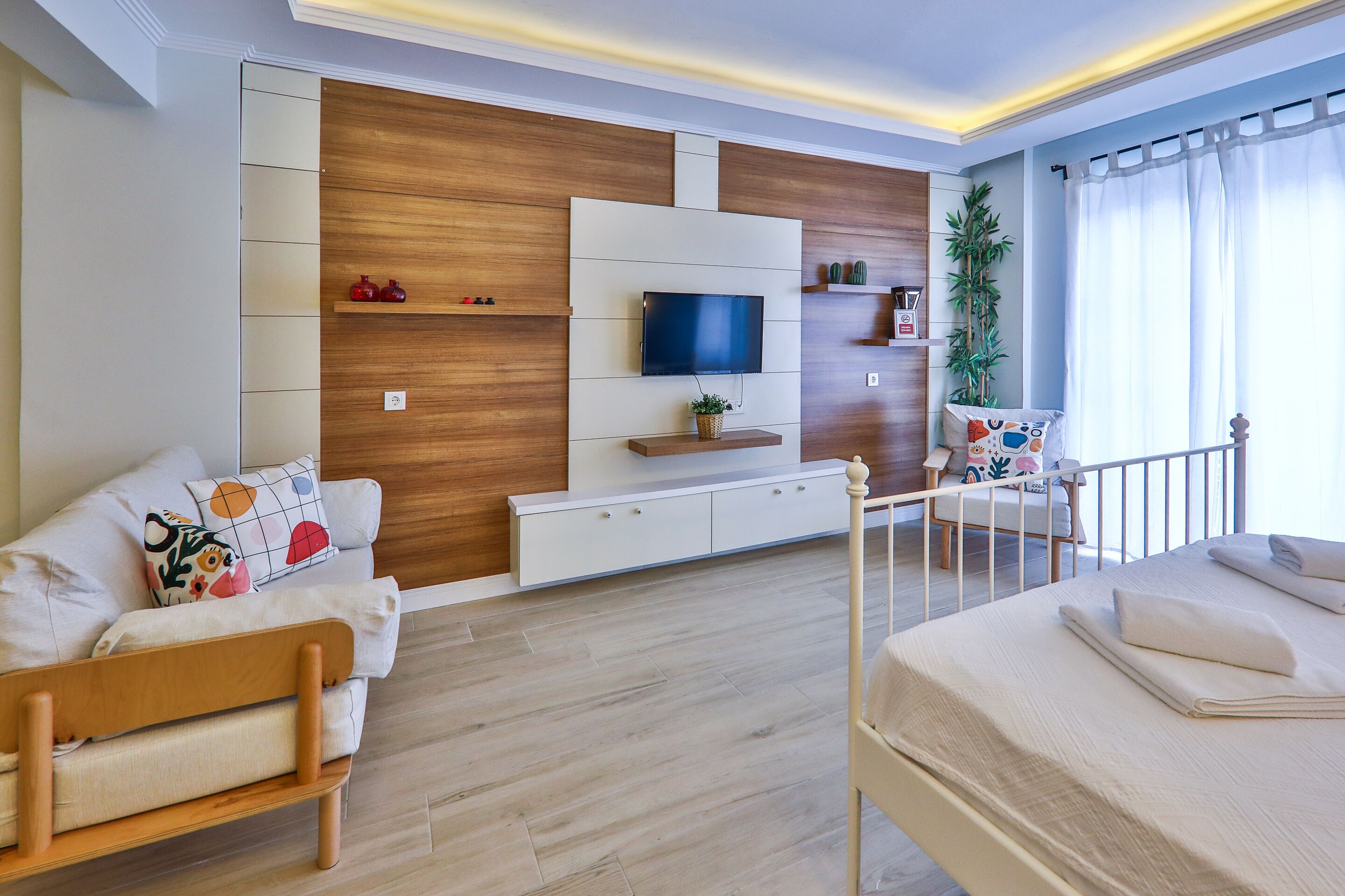Een moderne woonkamer met een bank, een bed, een televisie bevestigd aan een houten wand en een balkon met een hekwerk.