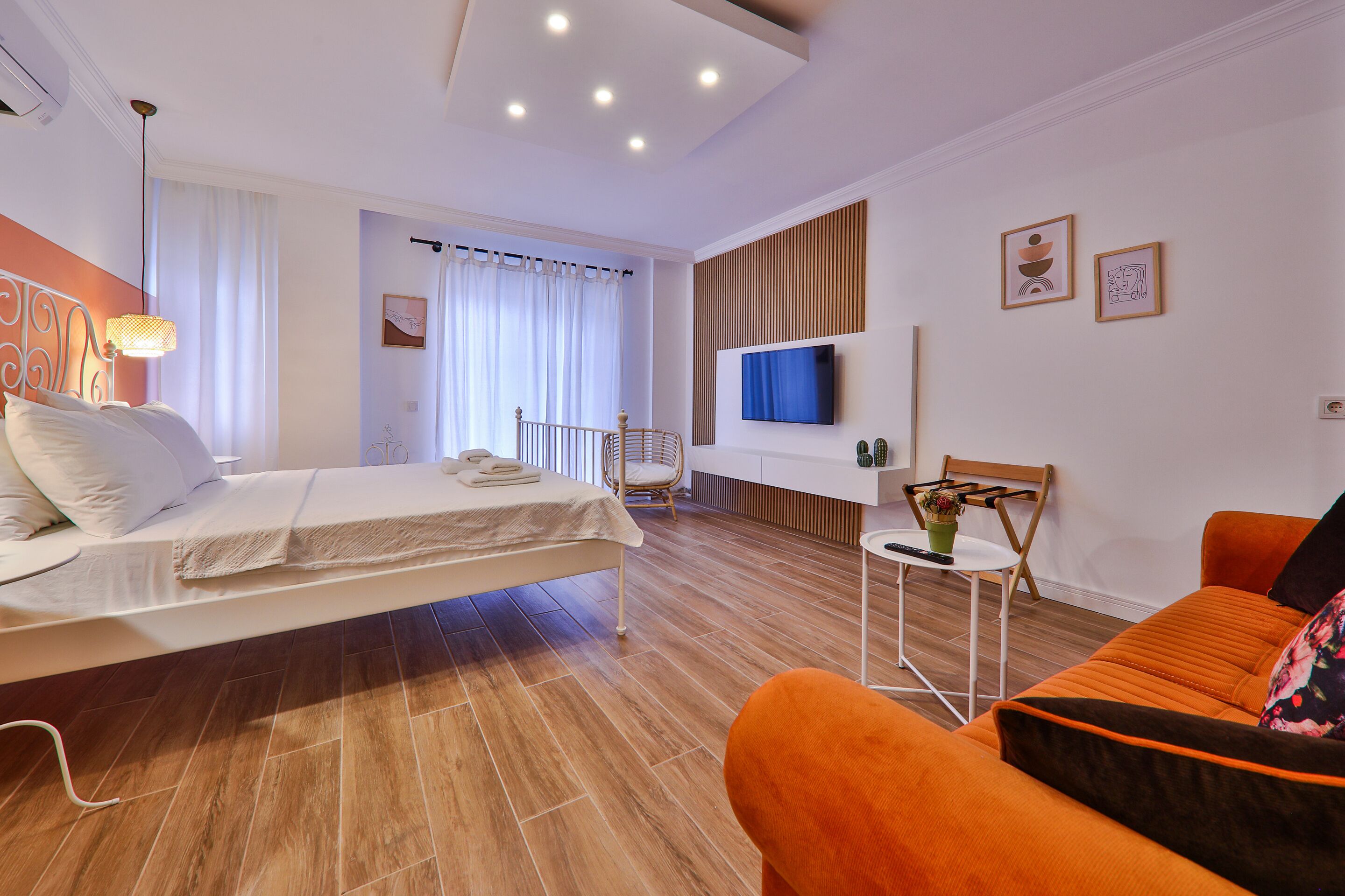 Une chambre d’hôtel moderne équipée d’un lit, d’un canapé, d’une télévision et d’une petite table agrémentée d’une plante.