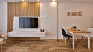 A modern living room with a flat-screen TV mounted on a white console, a dining table with chairs, and a wooden floor.