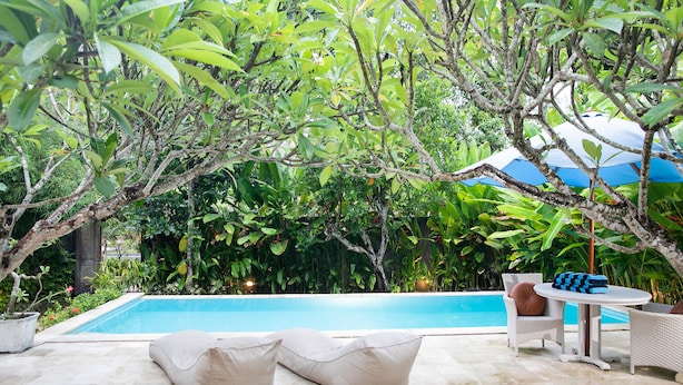 Una piscina rodeada de exuberante vegetación, con mobiliario exterior y una mesa.