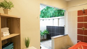 Un baño moderno con ducha, repisa de madera con toallas y una planta en maceta.