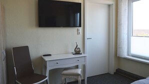 A hotel room with a desk, chair, TV, and a window with curtains.