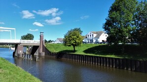 A river with a bridge, a grassy embankment, and a white building in the background.